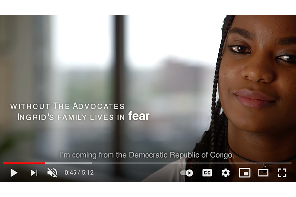 [ai] A close-up of a young woman with braided hair, speaking in a well-lit indoor setting. Text overlay states: 'Without The Advocates, Ingrid's family lives in fear.' She mentions her background from the Democratic Republic of Congo.